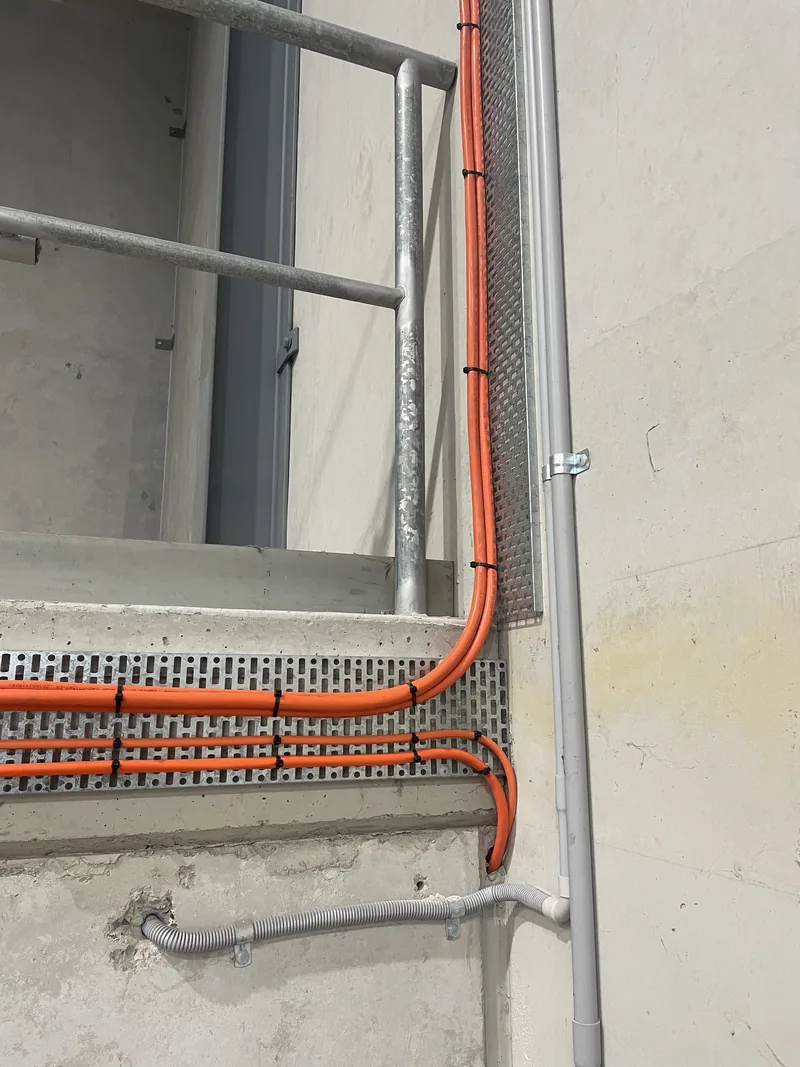 Orange conduit running into perforated cable tray along the precast wall